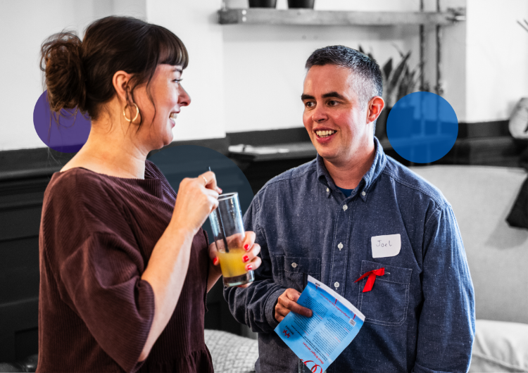Two people chatting warmly at a METRO social event, one holding an orange juice, both wearing name badges and appearing relaxed.
