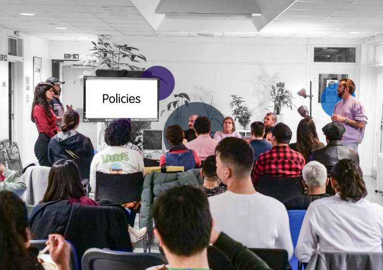 Community members gathered in METRO's meeting room for an educational session, with "Policies" displayed on screen, showing engaged attendees of diverse backgrounds.